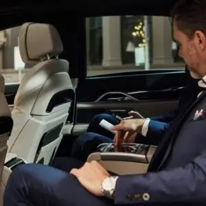 Two passengers in a luxury car, enjoying a comfortable ride with city lights visible outside.